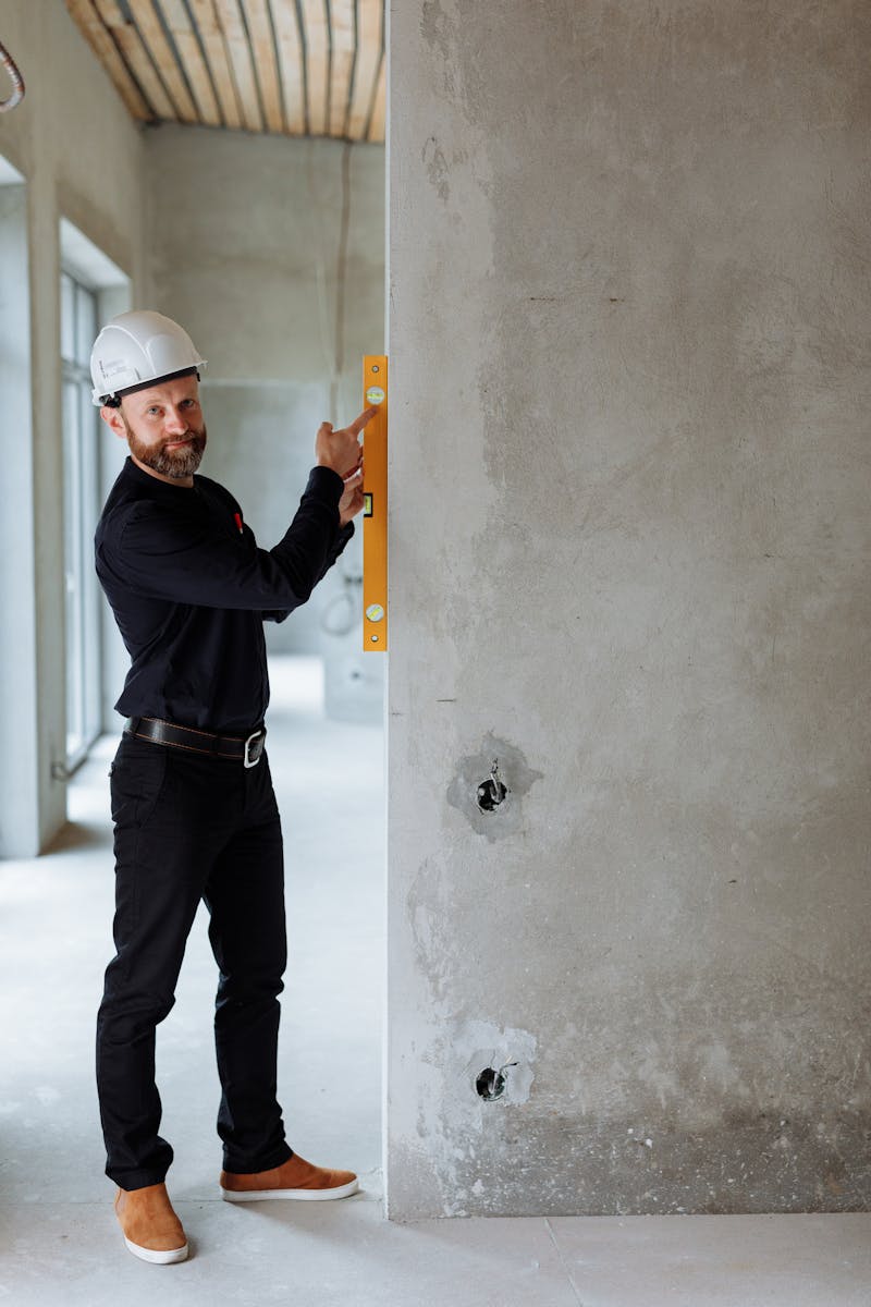 Smiling construction worker using spirit level on concrete wall at a building site.
